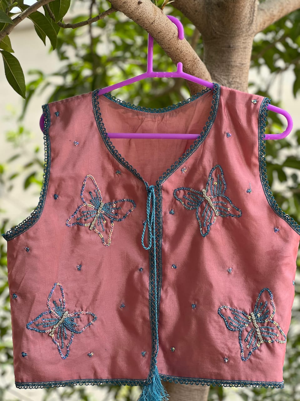 Front view of dusty rose butterfly embellished vest with teal trim and tassel ties
