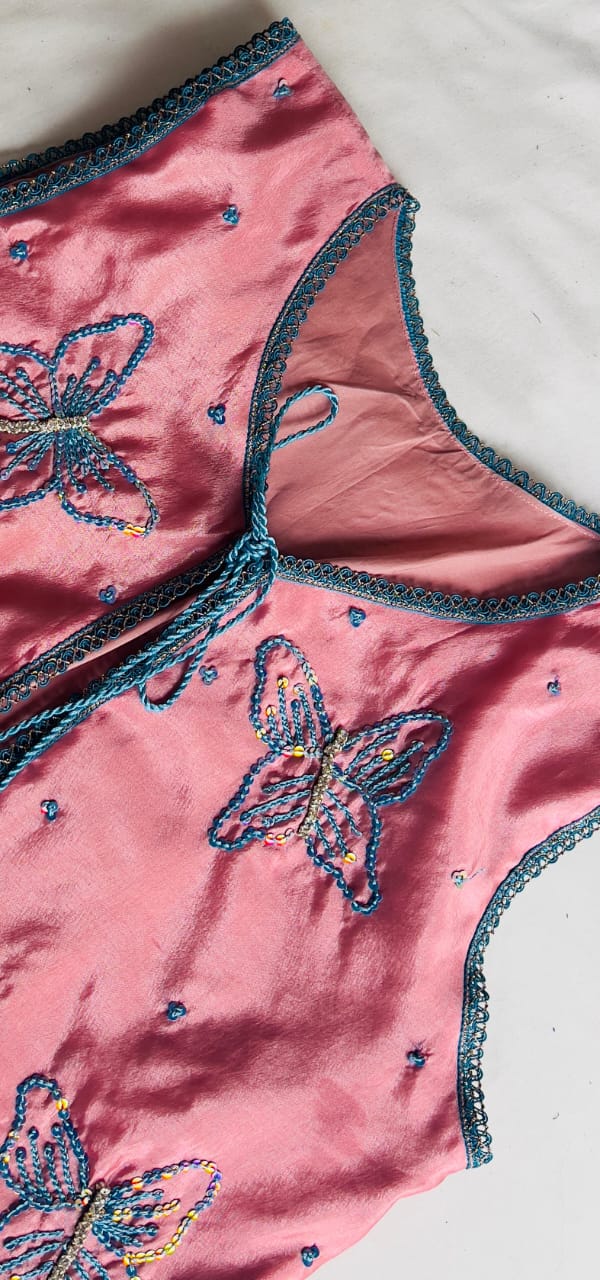 Detail of butterfly motifs and decorative teal edging on dusty rose vest