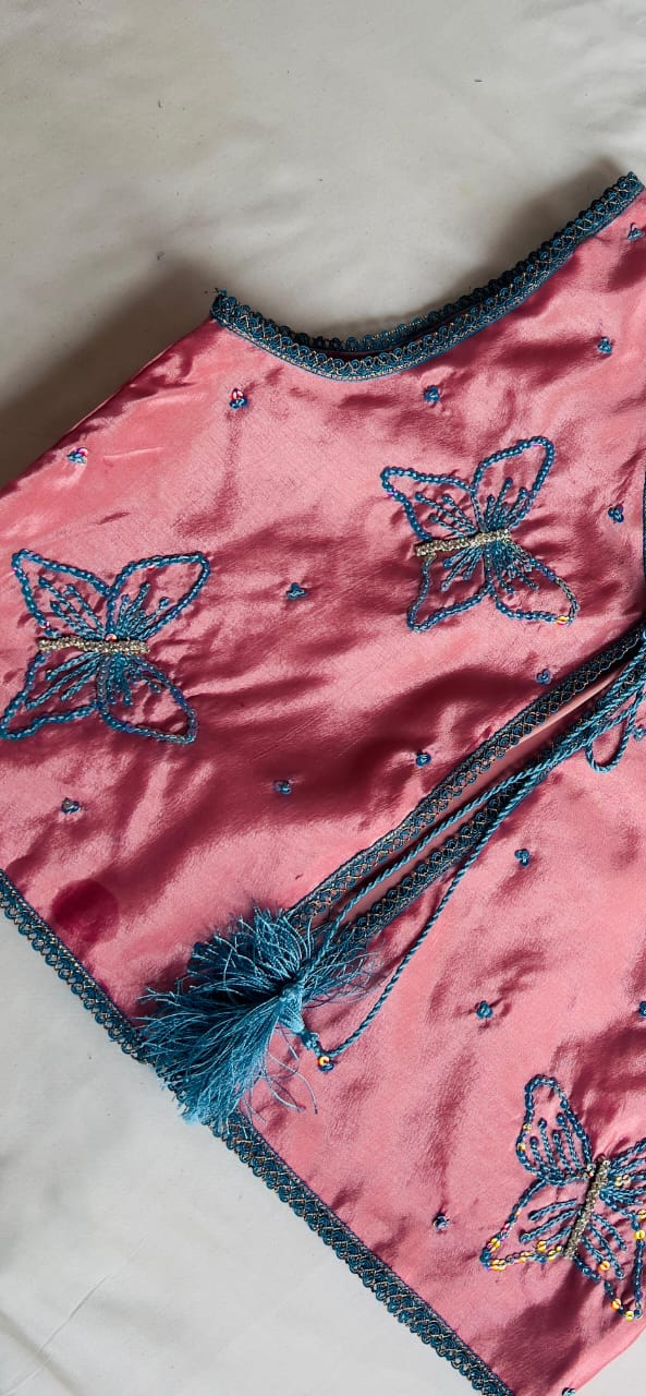 Close-up of butterfly embellishments and teal tassel ties on dusty rose vest
